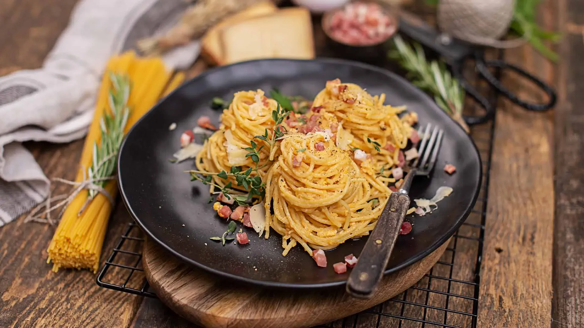 Tiroler Spaghetti Carbonara in drei Portionen mit Kräutern und Speck auf einem schwarzen Teller