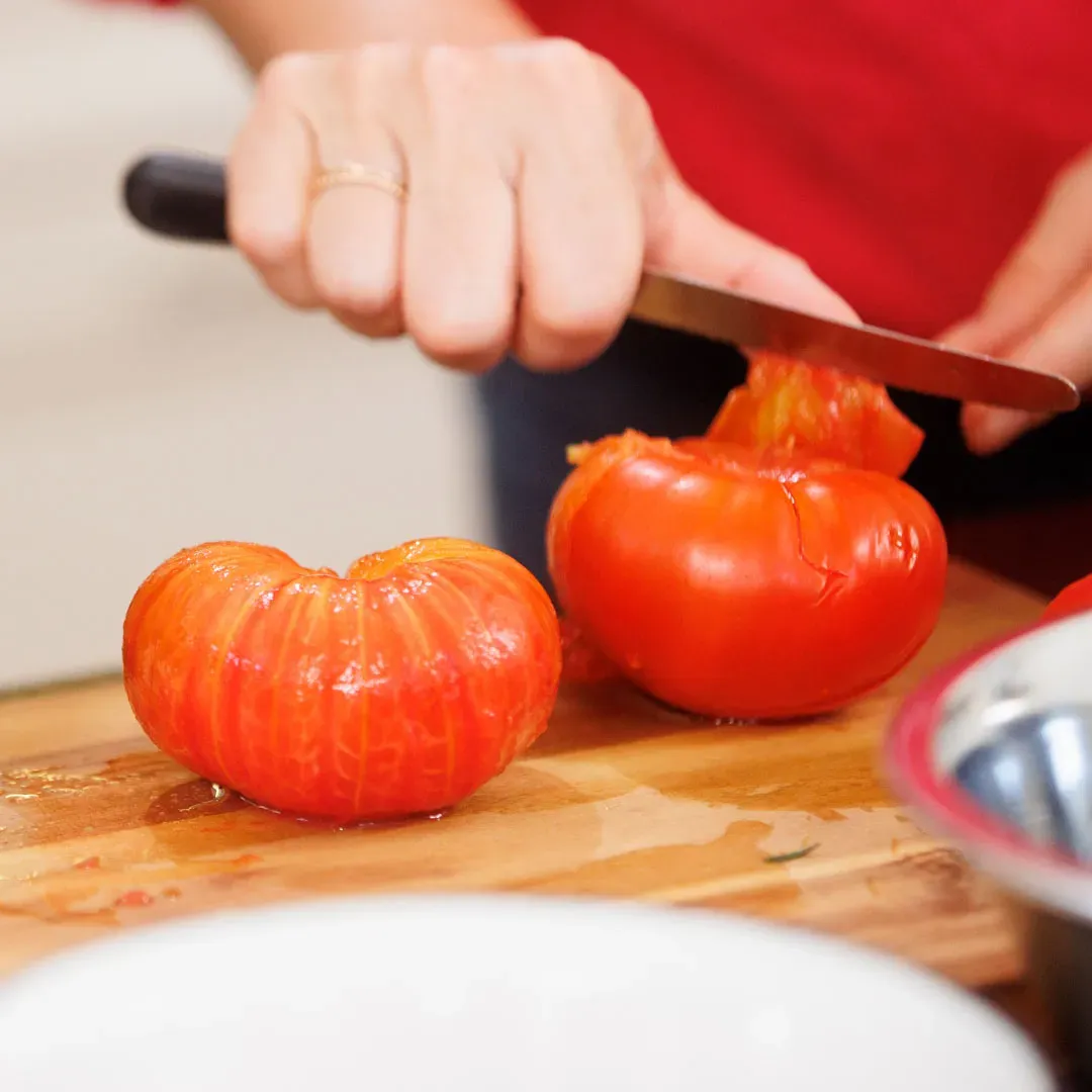 Hand schneidet gehäutete Tomaten mit einem Messer auf einem Holzbrett