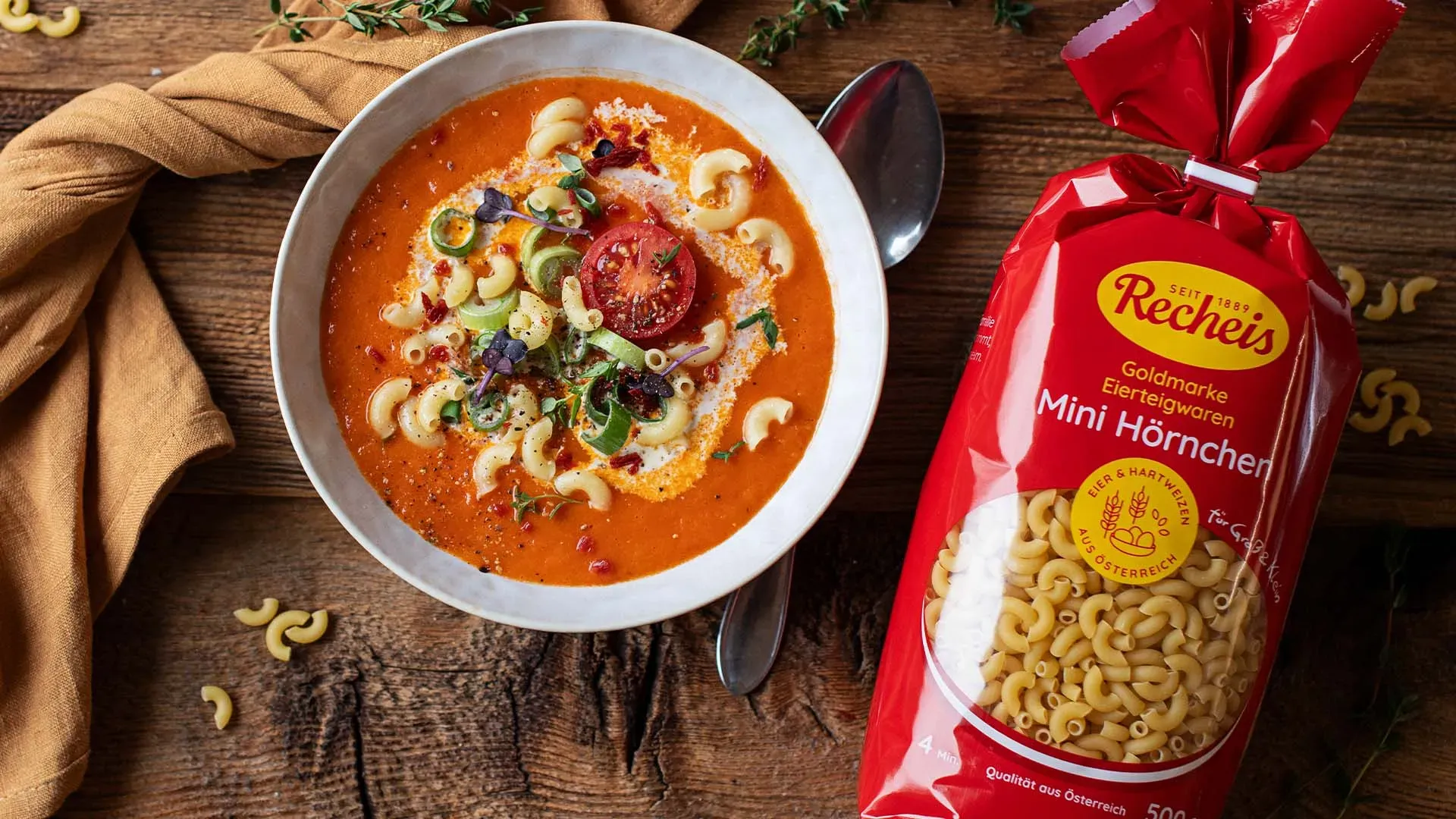 Schale Tomatensuppe mit Nudeln und Kräutern neben einer Packung Mini-Hörnchen