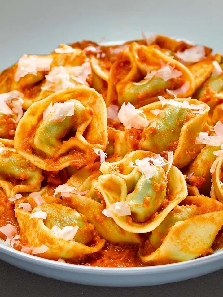 Nahaufnahme: Tortelloni mit Tomatensauce und verstecktem Gemüse, mit geriebenem Käse auf einem Teller