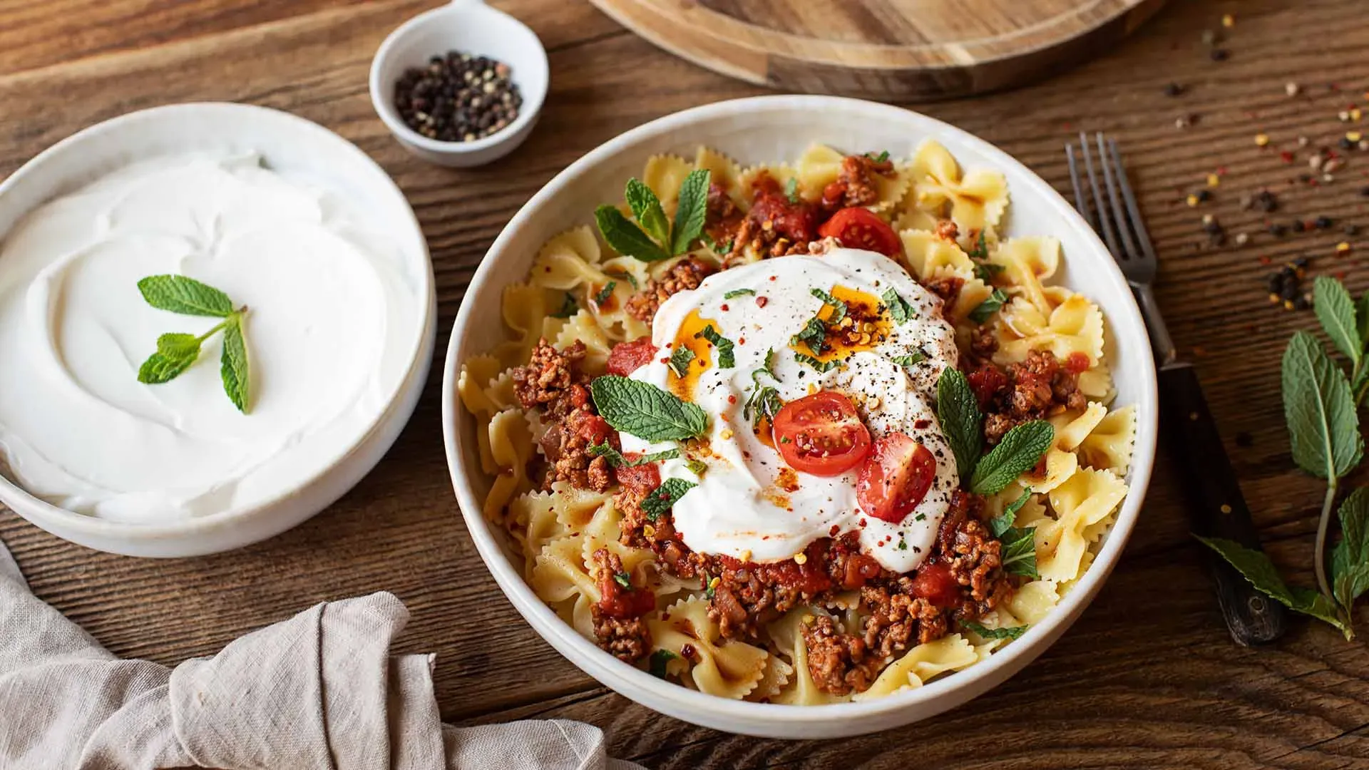 Türkische Nudeln mit Hackfleischsauce, Joghurt und Tomaten in einer Schüssel auf Holztisch