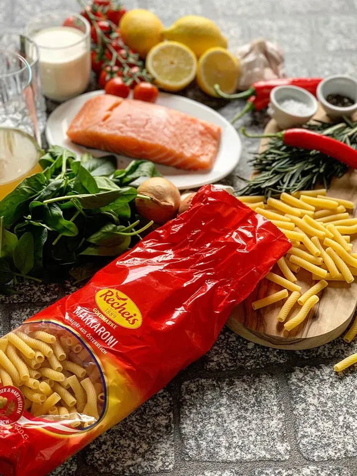 Zutaten für Valentinstagsrezept Makkaroni mit Gin-Sauce: Pasta, Lachs, Zitronen und frisches Gemüse auf einem Tisch