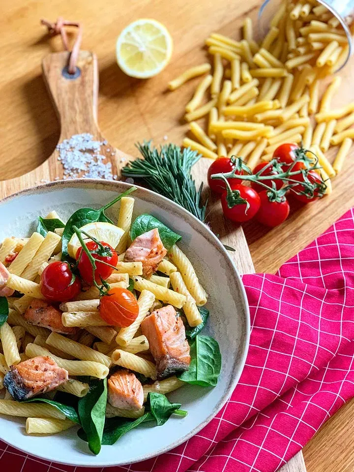 Valentinstagsrezept mit Nudeln und Lachs, Spinat und Kirschtomaten auf Holzbrett mit rotem Tuch