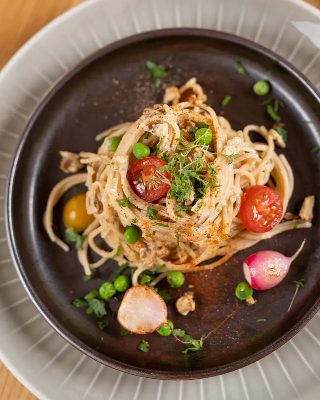 Vegane Spaghetti Carbonara mit Kirschtomaten, Erbsen und frischen Kräutern auf einem Teller