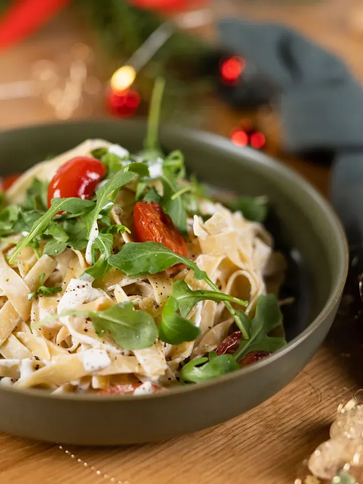 Vegane Frischkäsenudeln mit Vollkornbandnudeln, Rucola und Kirschtomaten in einer Schüssel auf Holztisch