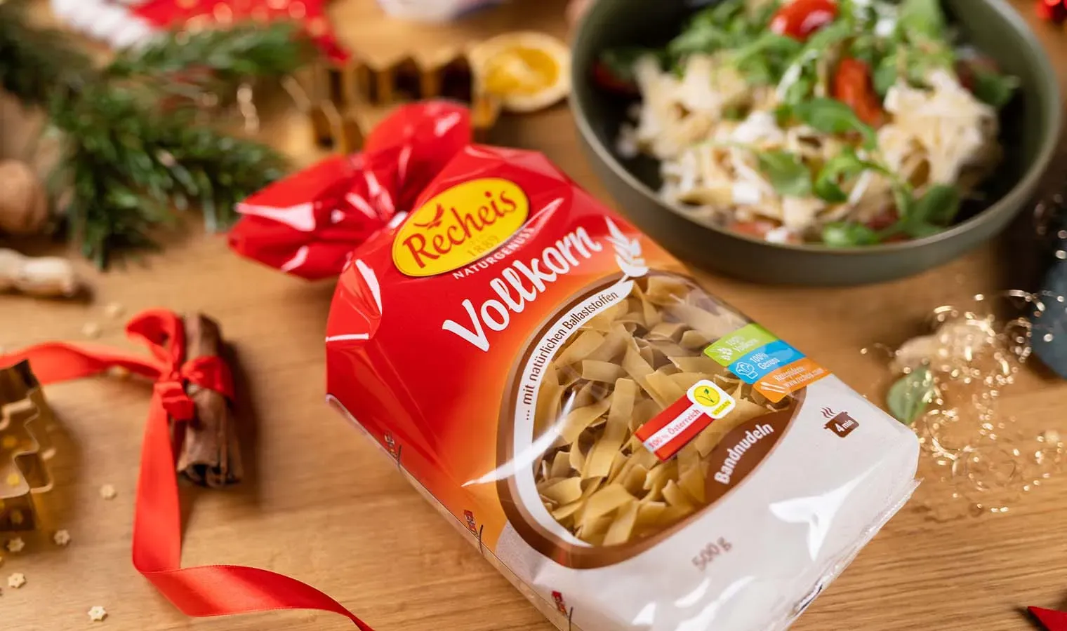 Packung Vollkornbandnudeln auf Holztisch mit Weihnachtsdeko und einem Teller vegane Frischkäsenudeln