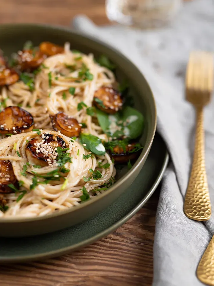 Vegane Jakobsmuscheln aus Kräuterseitlingen auf Spaghetti mit frischen Kräutern auf einem grünen Teller