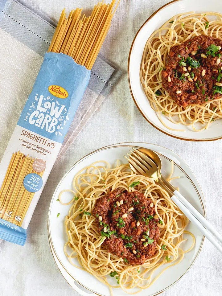 Vegane Low-Carb-Spaghetti Bolognese auf zwei Tellern neben einer Packung Low-Carb-Spaghetti