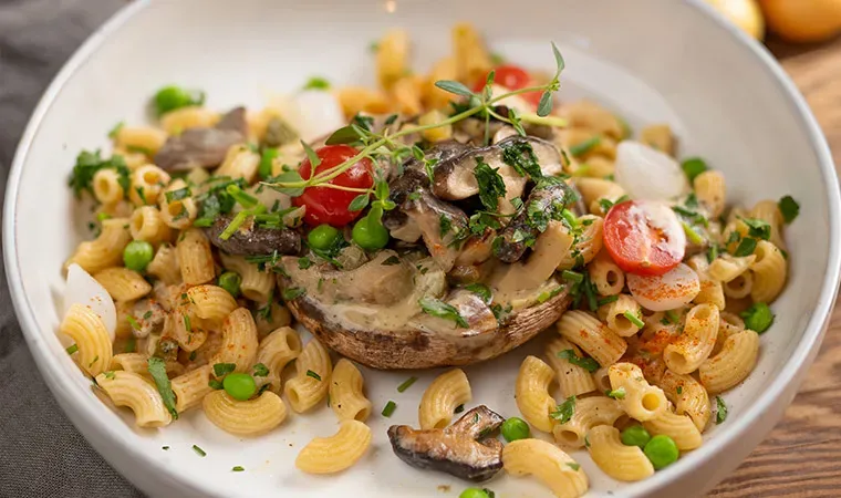 Vegane Pilzpfanne mit Pasta, Erbsen und Tomaten, serviert in einem gefüllten Portobello-Pilz mit Kräutern