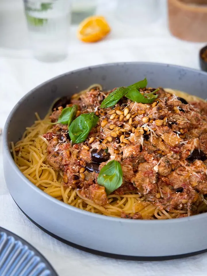 Vegane Spaghetti alla Norma mit Tomatensauce, Pinienkernen und Basilikumblättern auf einem Teller