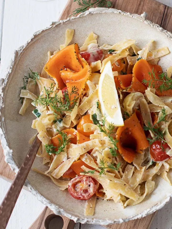 Nahaufnahme: vegane Lachsnudeln mit Vollkornbandnudeln, Karotten, Kirschtomaten, Dill und Zitronenscheibe in einer Schüssel
