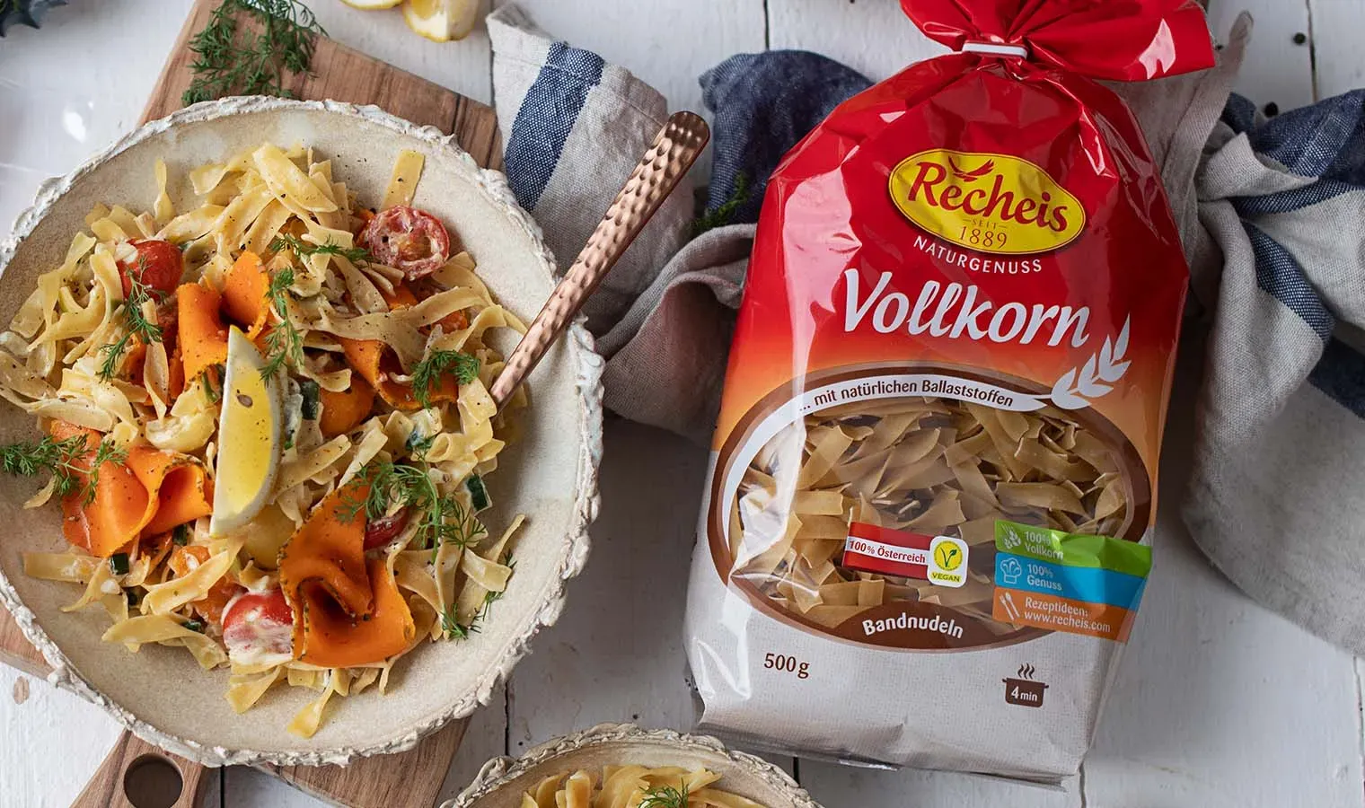 Vegane Lachsnudeln mit Vollkornnudeln und Gemüse in einer Schale neben einer Packung Recheis Bandnudeln, von oben