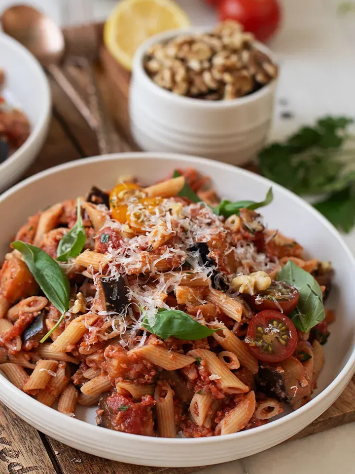 Veganes Bolognese mit Vollkorn-Penne in Tomatensauce mit Basilikum und geriebenem Käse auf einem Teller