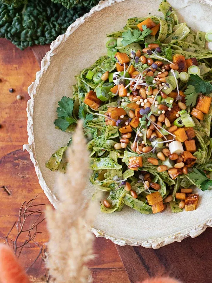 Veganes Pesto mit grüner Pasta und geröstetem Gemüse, garniert, auf Holztisch