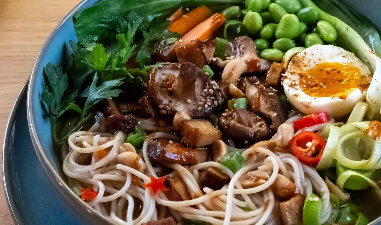 Nahaufnahme: vegetarische Ramen mit Spaghetti, Pilzen, Ei, Gemüse und Kräutern auf blauem Teller