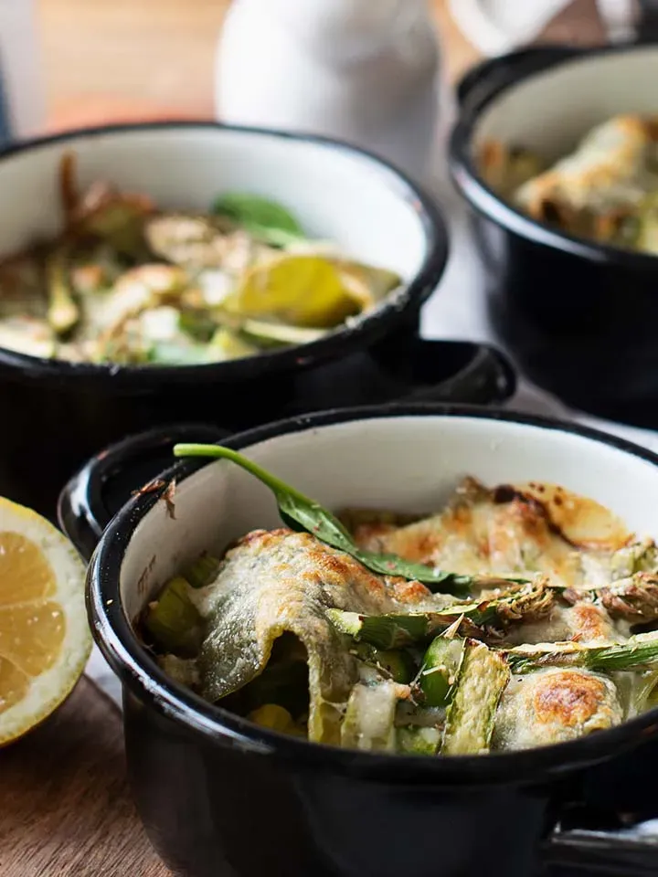 Nahaufnahme: vegetarische Spargel-Lasagne, überbacken in schwarzen Auflaufförmchen mit Zitronenscheibe