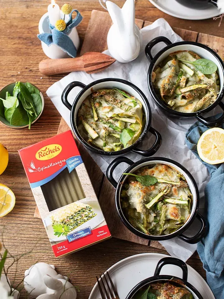 Vegetarische Spargel-Lasagne für Ostern in drei Auflaufförmchen mit frischen Zutaten auf Holztisch