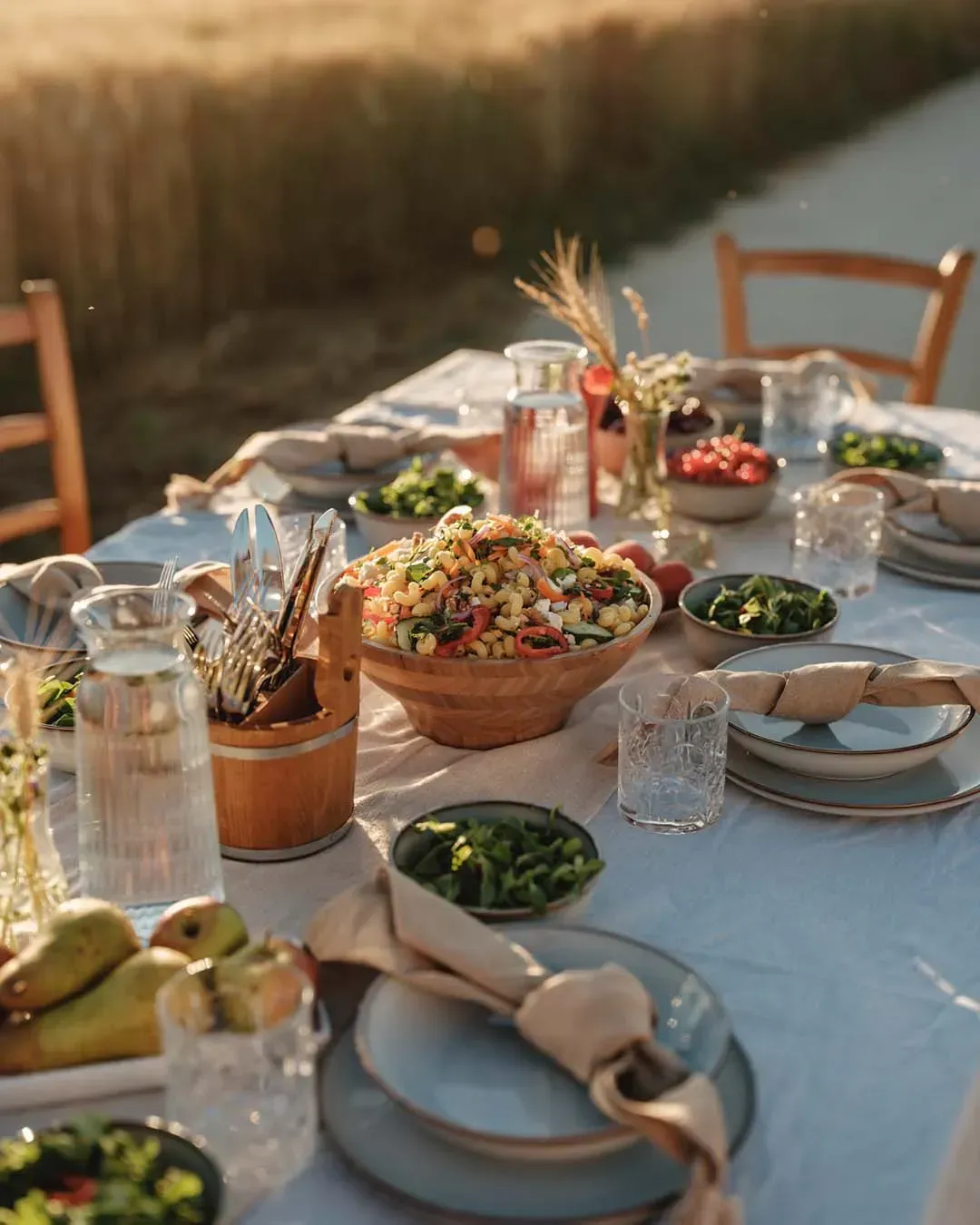 Gedeckter Tisch am Getreidefeld mit einer großen Holzschüssel voll vegetarischem Nudelsalat