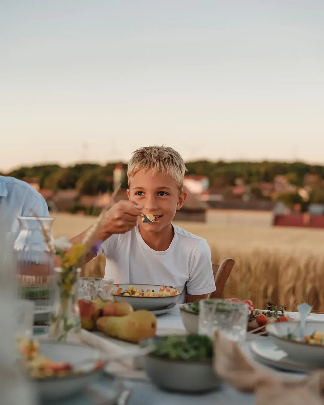 Ein Kind isst am Abendtisch im Freien vegetarischen Nudelsalat aus einer Schale