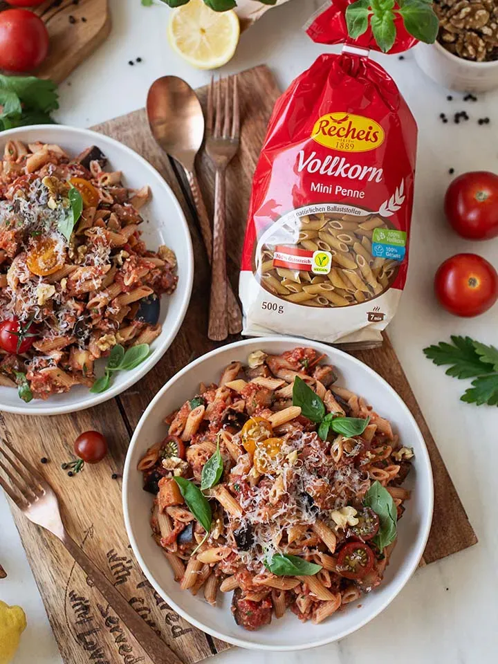 Vegane Bolognese mit Vollkorn-Mini-Penne in Tomatensauce, mit Basilikum und Käse auf zwei Tellern