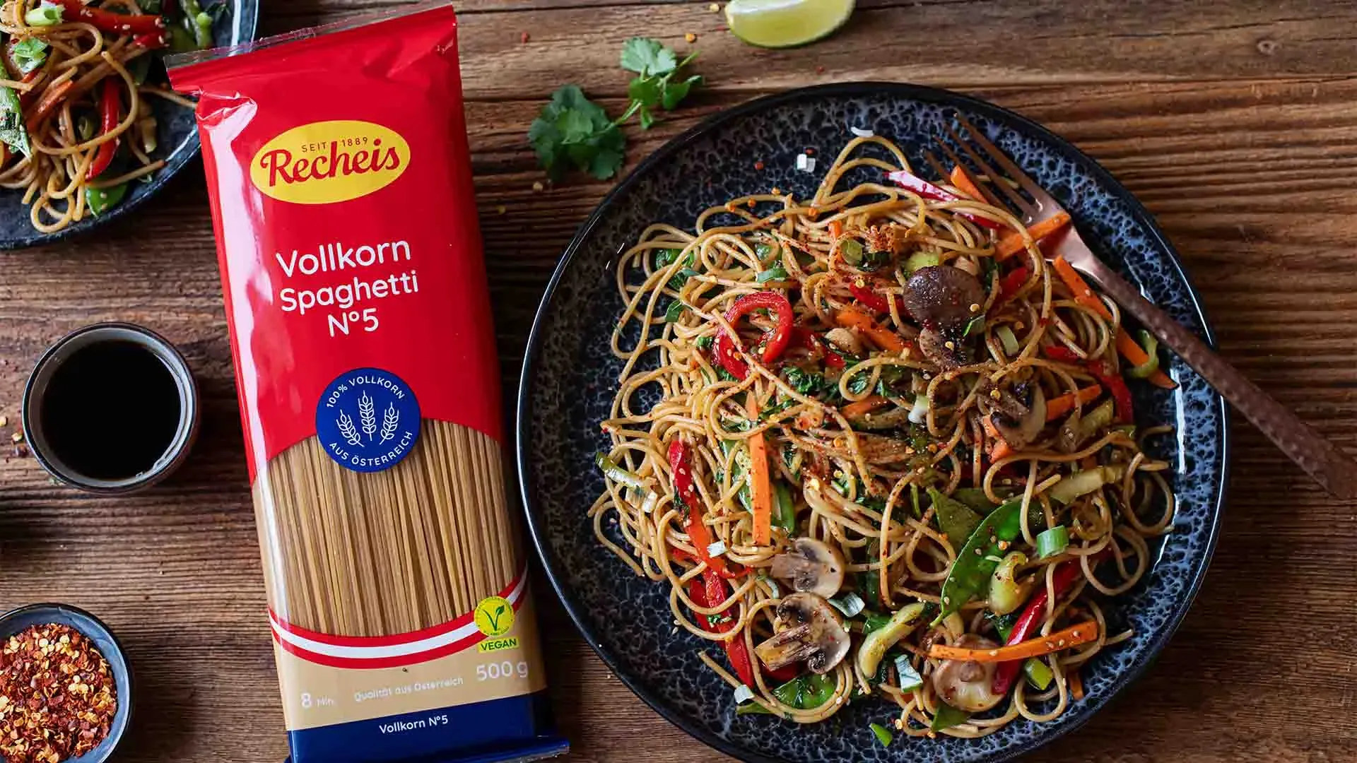 Vollkorn-Spaghetti Asia mit Gemüse auf einem Teller neben der Packung Vollkornspaghetti