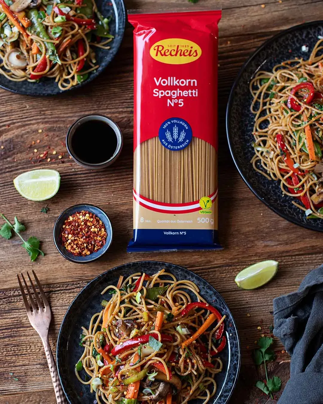 Vollkorn-Spaghetti mit würzigem Asiagemüse auf Tellern und Packung auf Holztisch