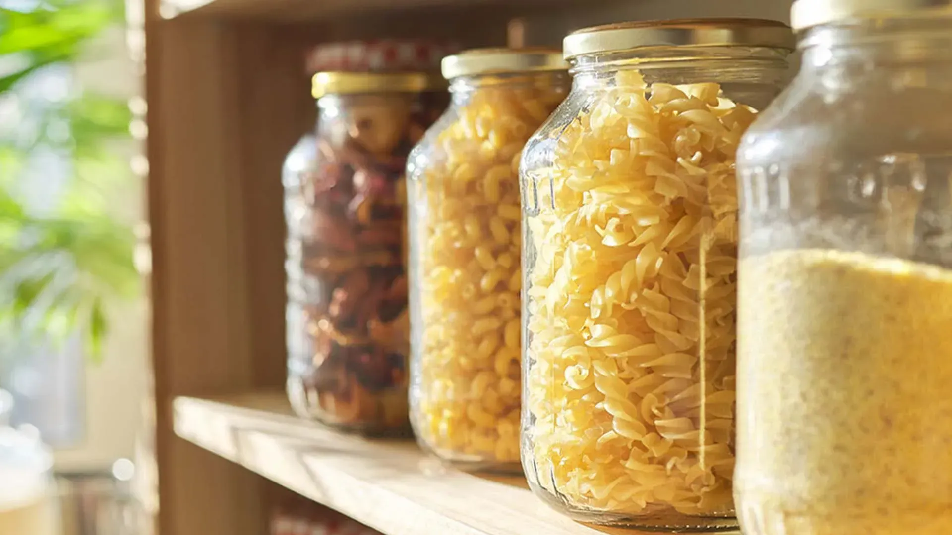 Glasbehälter mit Nudeln, Bohnen und Grieß in einem Holzregal