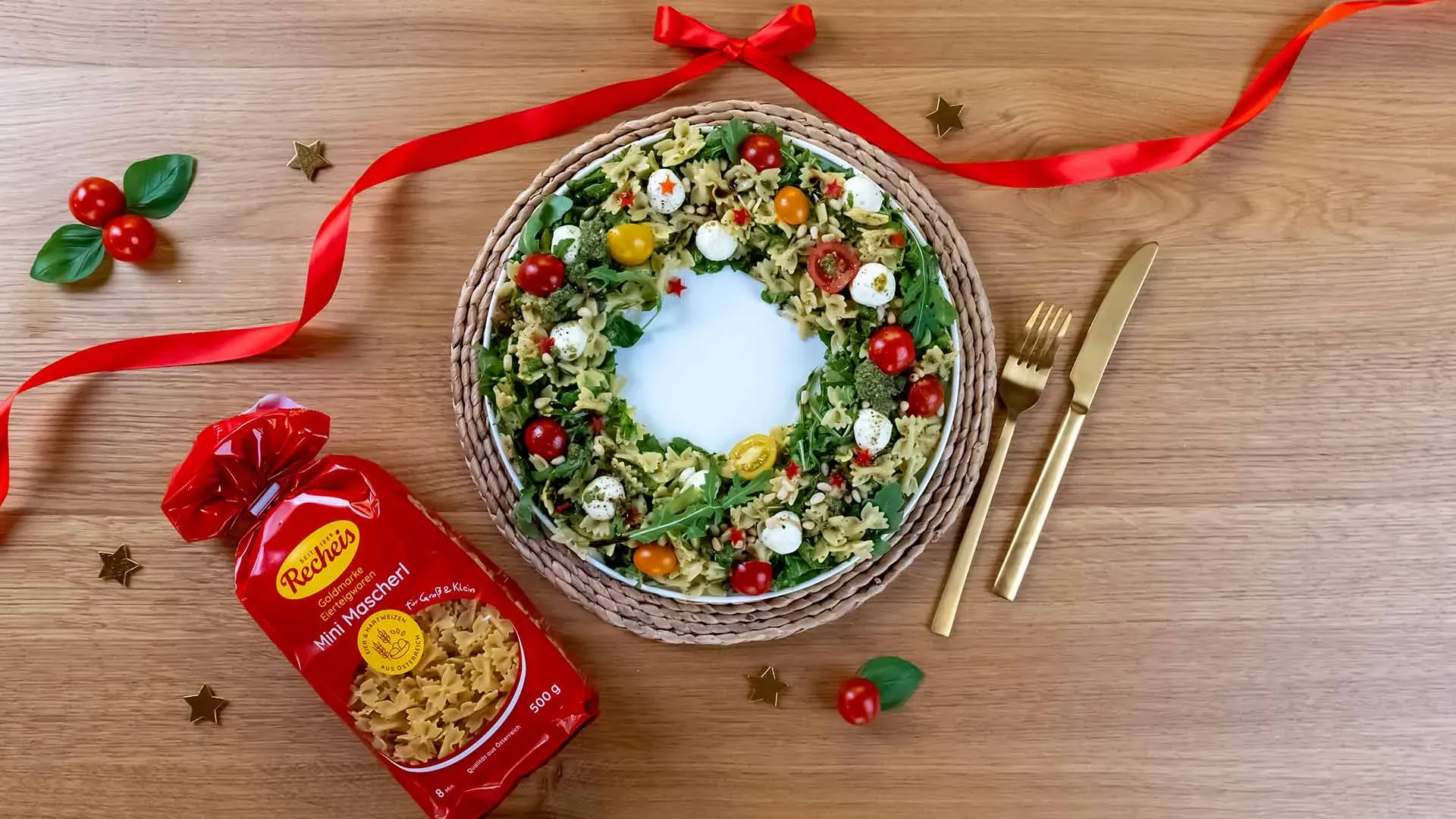 Weihnachtlicher Caprese-Nudelsalat-Kranz mit roten Schleifen und goldfarbenem Besteck