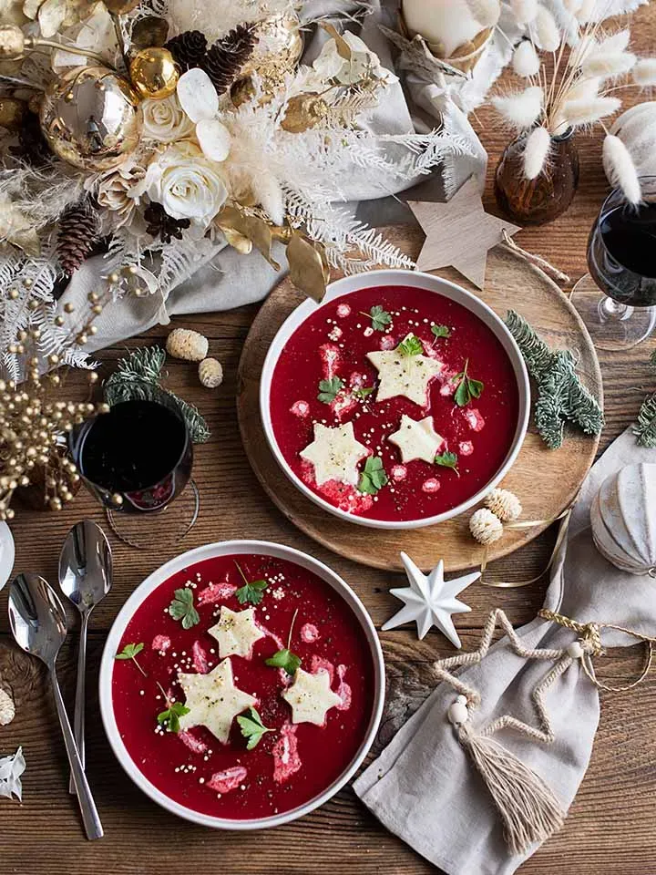 Weihnachtssuppe mit Roten Rüben: zwei Schalen rote Suppe mit sternförmigen Einlagen und weihnachtlicher Dekoration