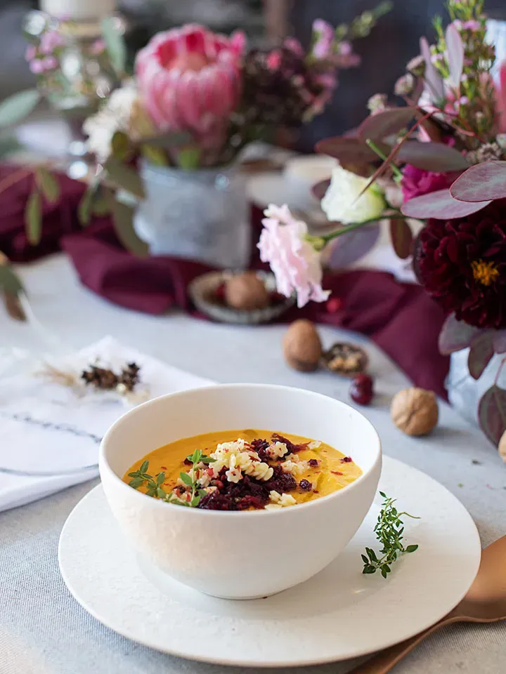 Weihnachtssuppe mit Nudeln in weißer Schüssel, dekoriert auf Tisch mit Blumen