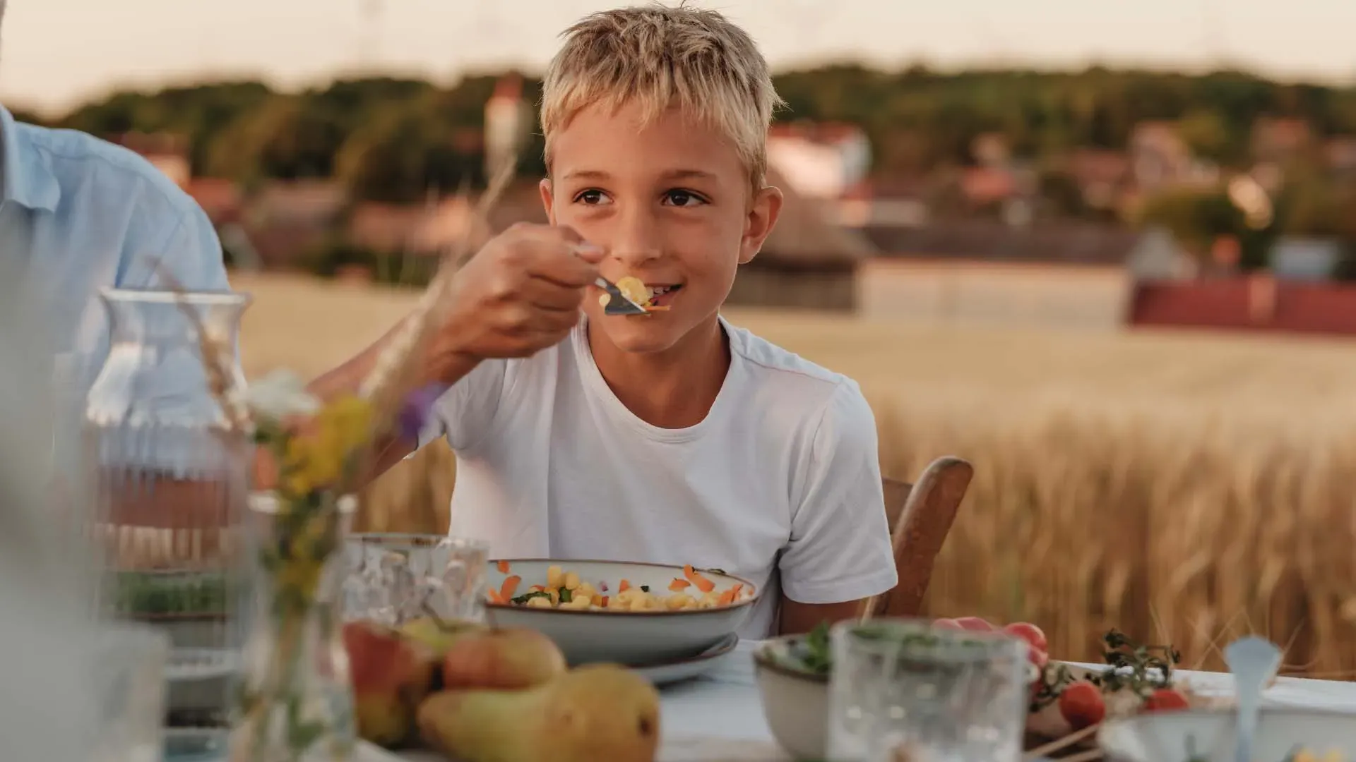Junge isst im Sommer draußen am Tisch mit Salat und Obst