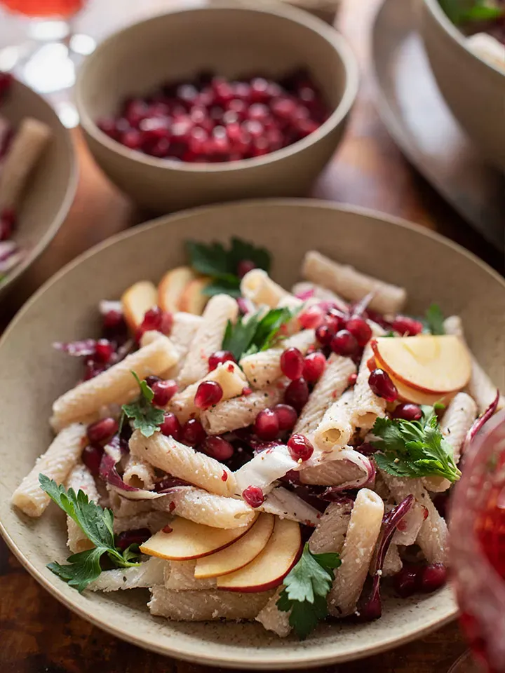 Winter-Nudelsalat mit Apfelscheiben, Granatapfelkernen und frischer Petersilie auf einem Teller