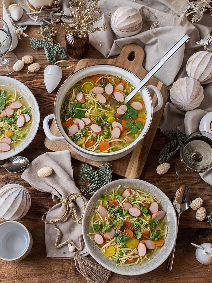 Würstelsuppe mit Nudeln auf Teller und im Topf auf festlich dekoriertem Holztisch