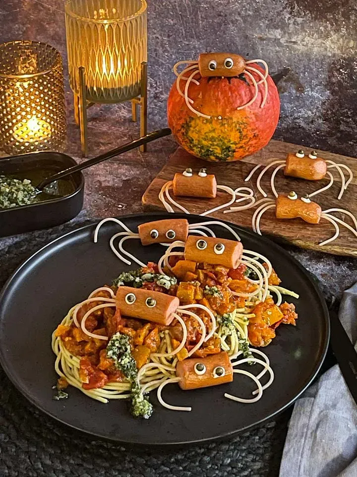 Würstlspinnen mit Kürbisragout: Spaghetti mit Würstchen-Spinnen und Kerzen auf dunklem Tisch