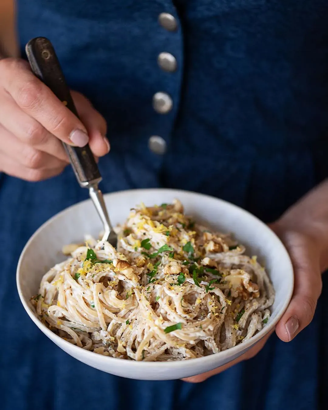 Person hält eine Schüssel Zitronennudeln mit cremigen Spaghetti und Kräutern in der Hand