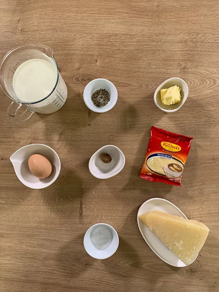 Zutaten für Glückssuppe: Milch, Ei, Butter, Gewürze, Käse und Grieß auf Holzuntergrund