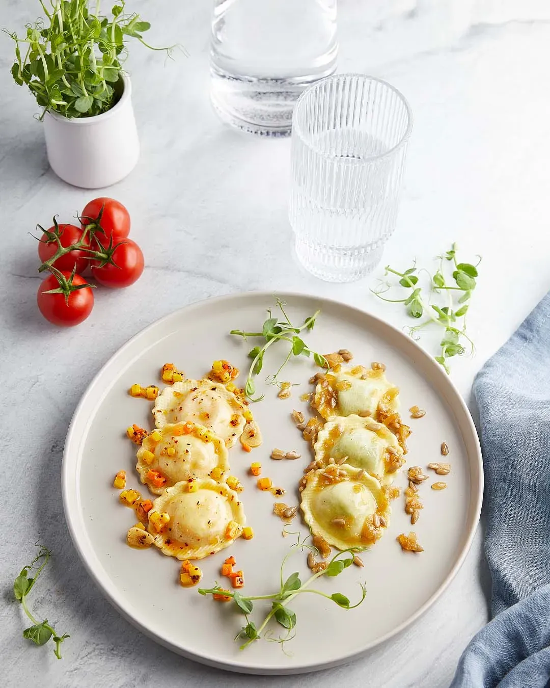 Zweierlei Fiori: Teller mit zwei Sorten Ravioli, garniert mit Kräutern und Gemüse, auf weißem Tisch